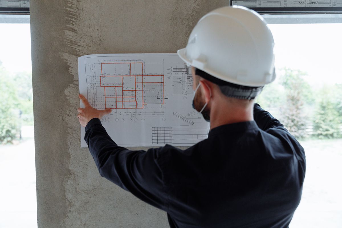 Director responsable de obra cotejando el plano estructural contra una columna de concreto en la obra